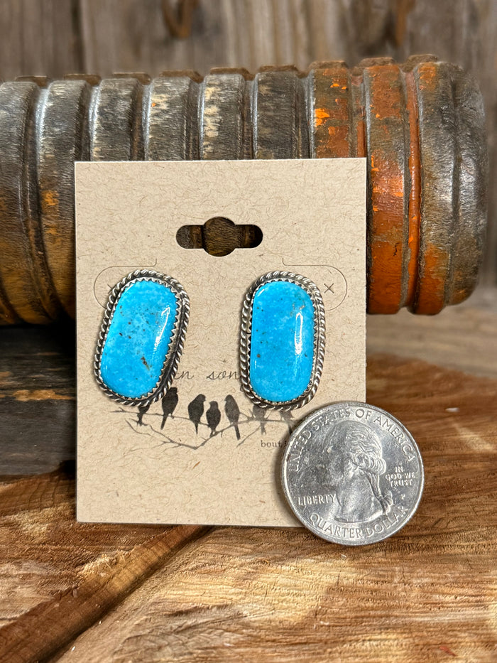 Turquoise oval stud earrings with silver border beside quarter coin on card