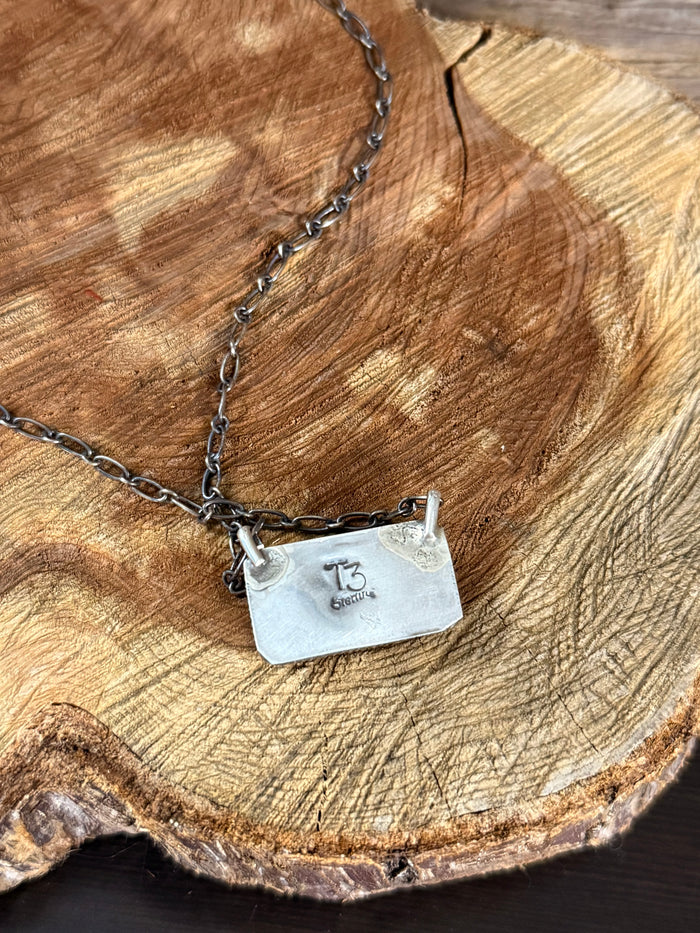 Silver chain necklace with rectangular pendant; back shows engraved lettering