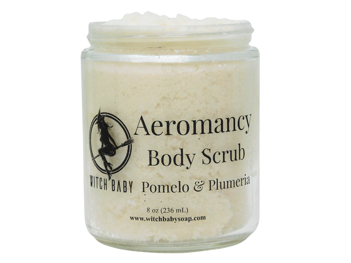 A clear glass jar of Witch Baby Aeromancy Body Scrub with a white lid, filled with a pale cream-colored scrub. The front label features black text and a witch silhouette logo.