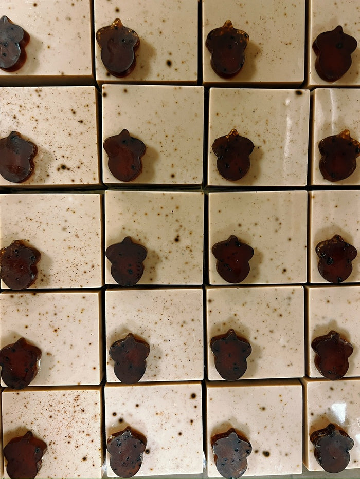 A grid of square coffee colored soaps, each decorated with a small dark brown acorn-shaped embellishment, photographed from above.