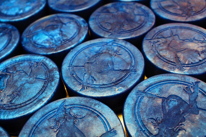 A close-up of multiple round, dark blue soaps or discs with embossed witch illustrations, arranged tightly together.
