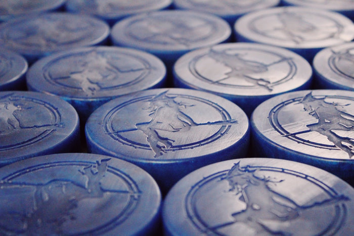A close-up, angled view of multiple round blue soaps arranged in rows, each embossed with a witch-like figure riding a broomstick.