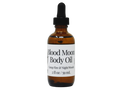 brown glass dropper bottle with white label that reads blood moon  body oil. camp fire & night woods.