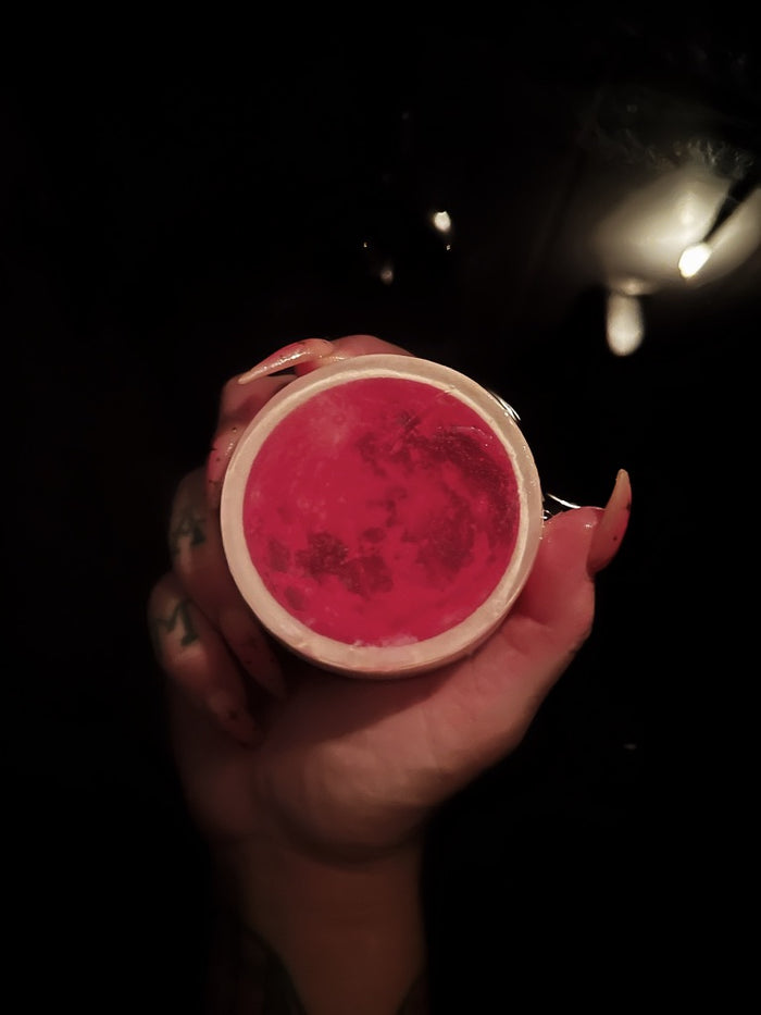 A hand holding a red moon soap against a black bath in the background