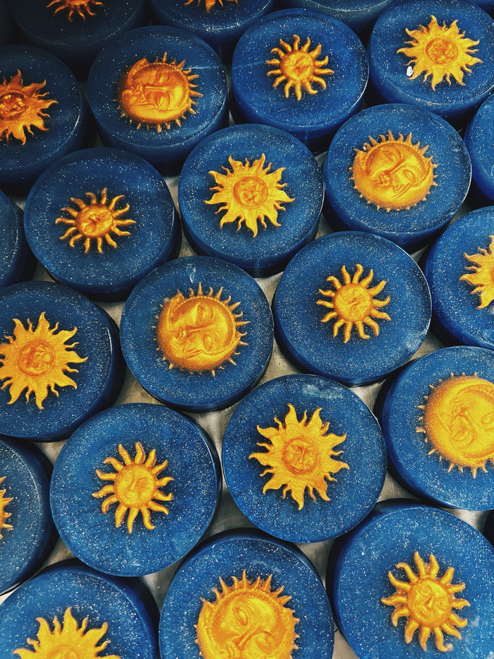 A close-up arrangement of round blue soaps, each decorated with a raised yellow sun motif in the center.
