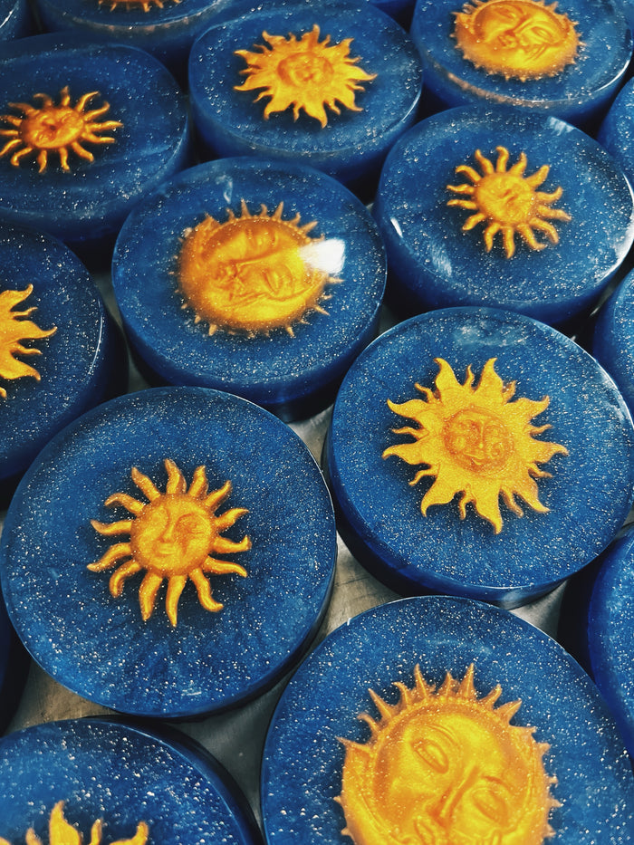 A close-up of multiple round blue soap bars arranged together, each featuring a raised yellow sun design on top.