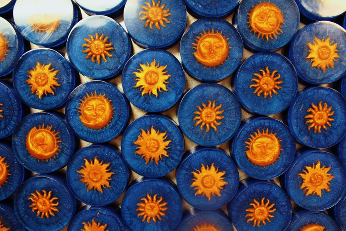 A close-up, top-down view of multiple round blue soaps arranged in a grid, each featuring a raised orange sun design in the center.