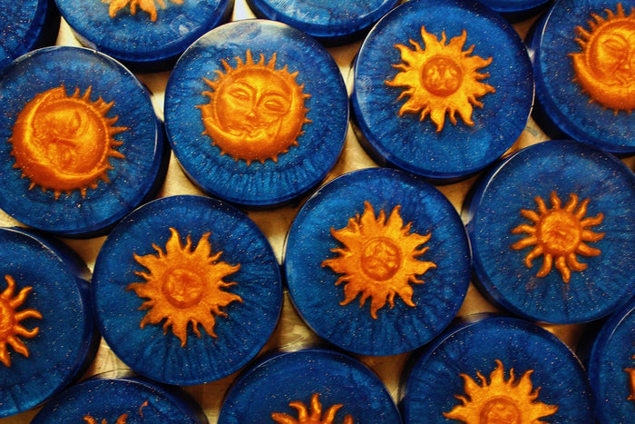 A close-up arrangement of round blue soaps, each featuring a raised orange sun design with a small face in the center.