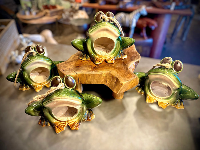 Multiple ceramic frog birdfeeders displayed on a rustic wood stand in store, showing glaze variation across handcrafted pieces