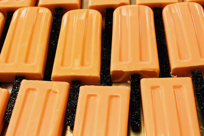 Close-up of multiple orange popsicle-shaped soaps arranged in rows on a dark textured surface.