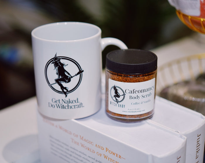 A white ceramic mug and a small jar of body scrub displayed together on a white surface. The mug has a black witch graphic and the text 'Get Naked.
