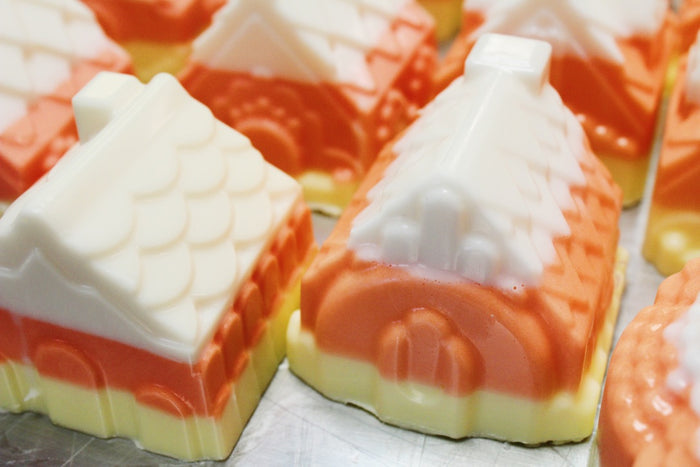 Candy corn house-shaped soaps with orange, white, and pale yellow layers, arranged closely together on a metallic surface.