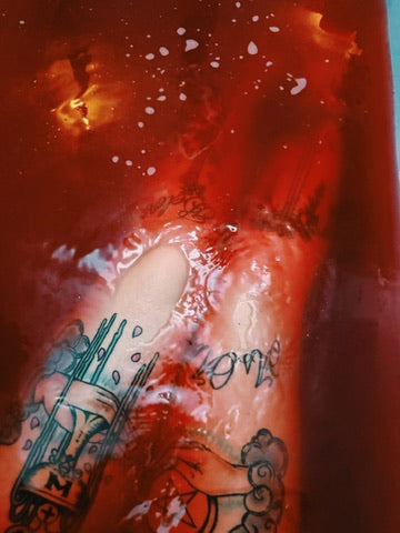 A close-up of tattooed legs covered in red bathwater, with visible black and gray tattoo designs and the word 'love' written across the skin.