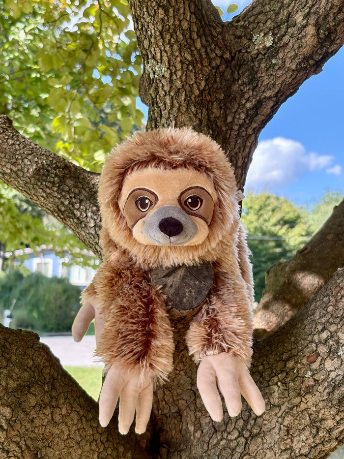 Earth Keeperz sloth plush posed upright in the fork of a tree branch outdoors, showing fully posable body and realistic brown fur