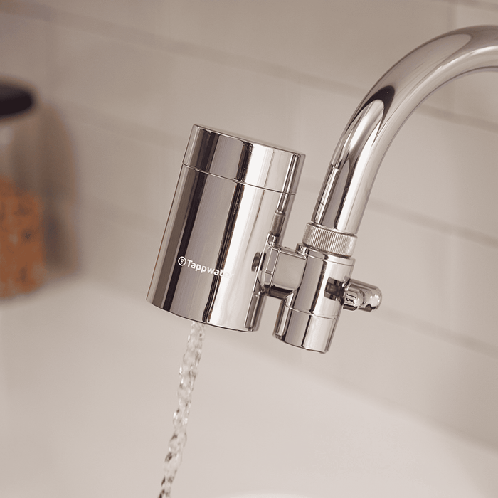 Chrome Tappwater filter attached to a kitchen faucet with water flowing.