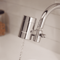 Chrome Tappwater filter attached to a kitchen faucet with water flowing.