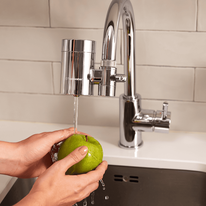 Person washing a green apple under running water from a kitchen faucet.