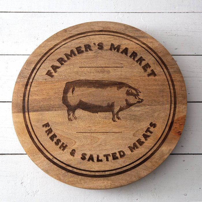 18-inch Farmer's Market wood lazy susan with hand-engraved pig motif displayed on a rustic dark wood farmhouse table, styled with linen napkin, fresh lavender, and rosemary sprigs — spinning turntable centerpiece for farmhouse dining tables