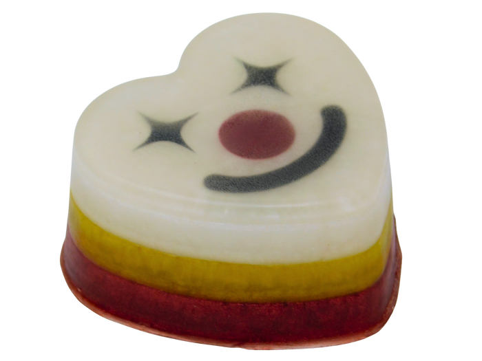 A heart-shaped layered soap with a white top layer decorated with a black smiley clown face and star details, layered over yellow and red bands, on a plain white background.