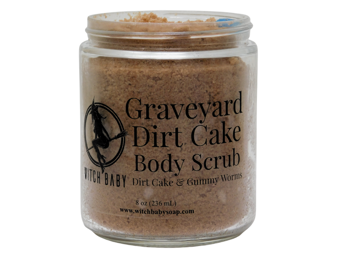 A clear glass jar of Witch Baby Graveyard Dirt Cake Body Scrub, showing the brown scrub inside, on a solid white background.