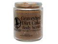 A clear glass jar of Witch Baby Graveyard Dirt Cake Body Scrub, showing the brown scrub inside, on a solid white background.