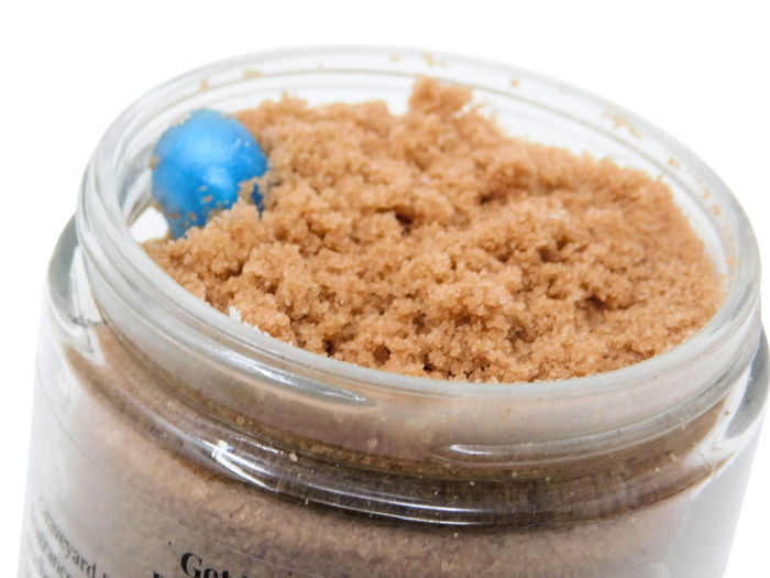 An open clear glass jar filled with coarse brown body scrub, with a soapy gummy worm visible inside near the rim, on a white background.