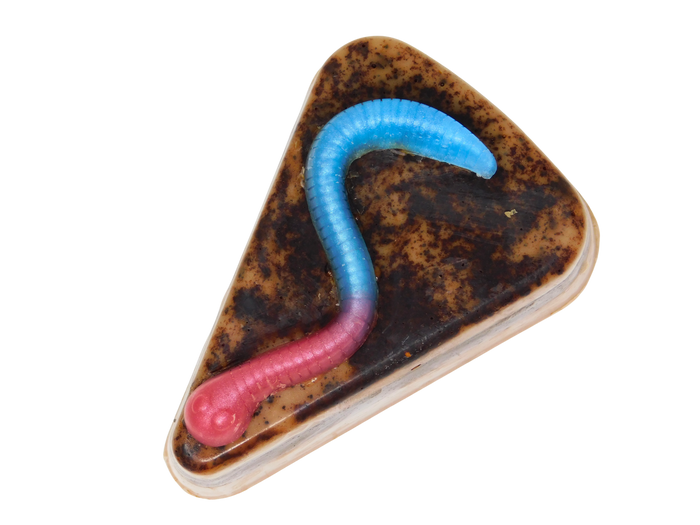 A cake slice shaped soap with a realistic gummy worm with a blue-to-pink gradient body, set against a plain white background.