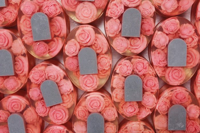 A close-up, top-down view of multiple ovalsoaps filled with pink rose-shaped elements and a gray tombstone accent, arranged in a repeating pattern.