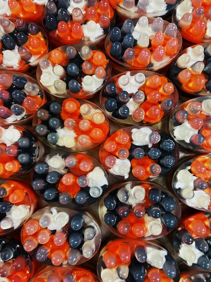 A close-up, top-down view of multiple clear massager soaps filled with a colorful halloween mixture of orange, black and white halloween shapes