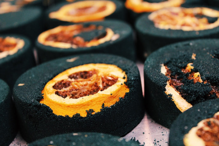 Close-up of several dark charcoal-bath bombs items with lemons, arranged closely together on a light surface.