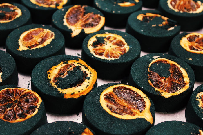 Close-up of sliced dark charcoal black bath bombs with dried lemons arranged closely together on a light surface.