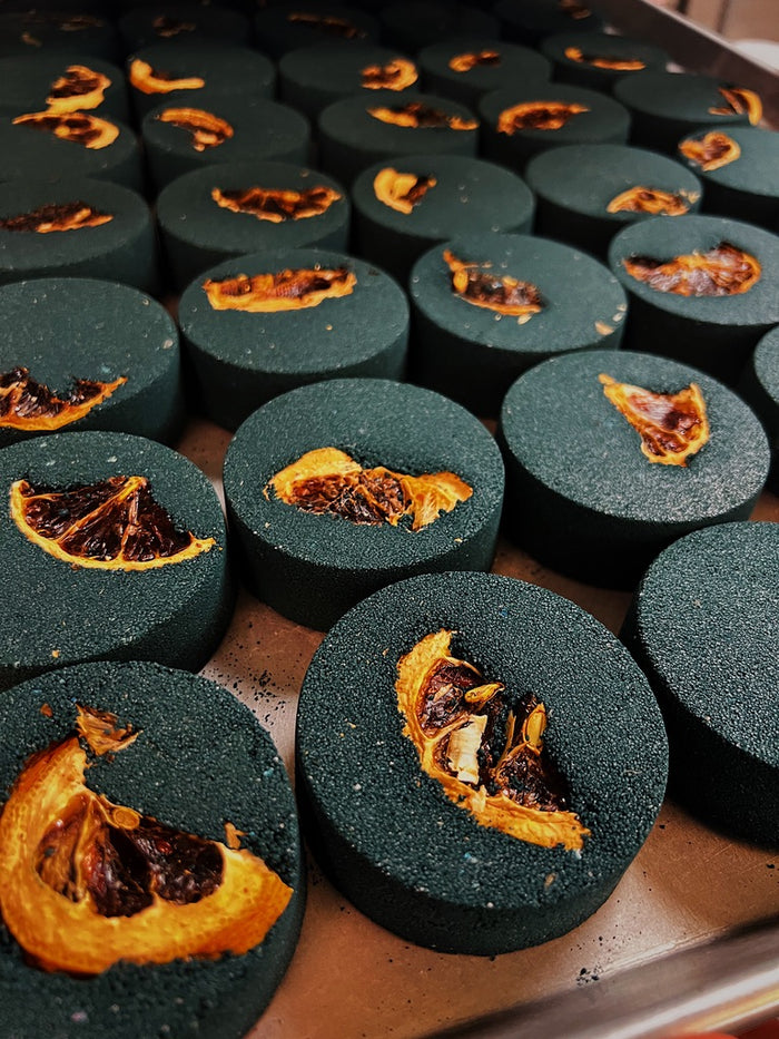 Close-up of sliced dark charcoal black bath bombs with dried lemons arranged closely together on a light surface.