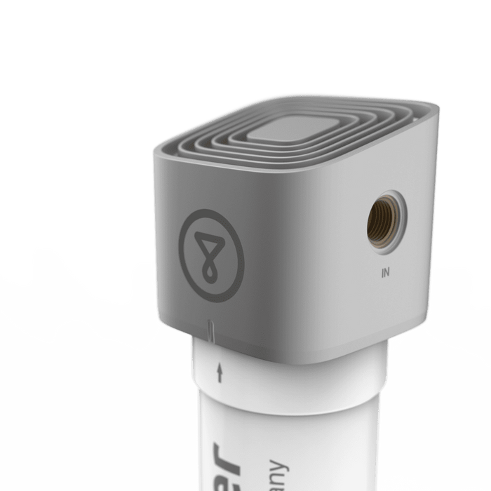 A close-up of the Tappwater Inline Filter SMR—a gray, square device with rounded edges, a circular logo, IN port, and mounted on a white cylindrical base with an upward arrow.