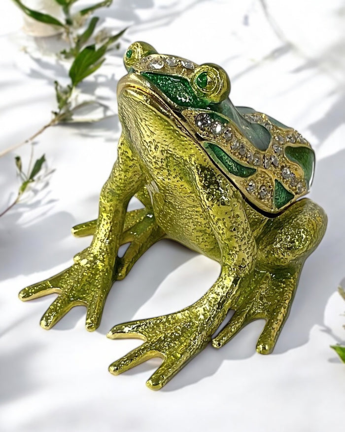 Gold tone green enamel frog trinket box with rhinestone detailing displayed on a white cloth with soft green botanical background