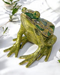 Gold tone green enamel frog trinket box with rhinestone detailing displayed on a white cloth with soft green botanical background