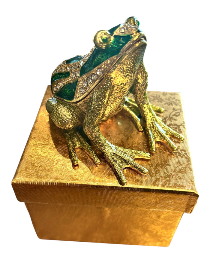 Jeweled green enamel frog trinket box displayed on top of a gold brocade gift box on white background