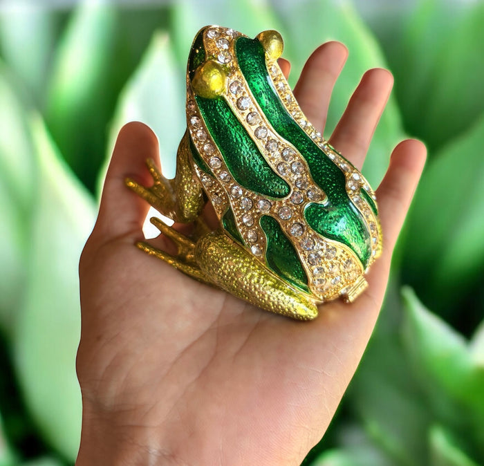 Hand held green enamel frog trinket box showing rhinestone back detail and swirling green enamel pattern against green leaf background