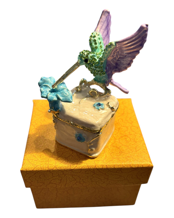 Jeweled hummingbird trinket box nestled inside open gold brocade gift box with orange satin lining, white background