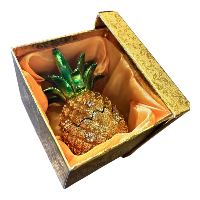 Gold enamel pineapple trinket box nestled inside open gold brocade gift box with orange satin lining, white background