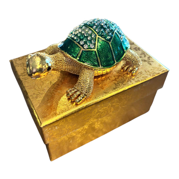 Jeweled tortoise trinket box with emerald green rhinestone shell displayed on top of gold brocade gift box, white background