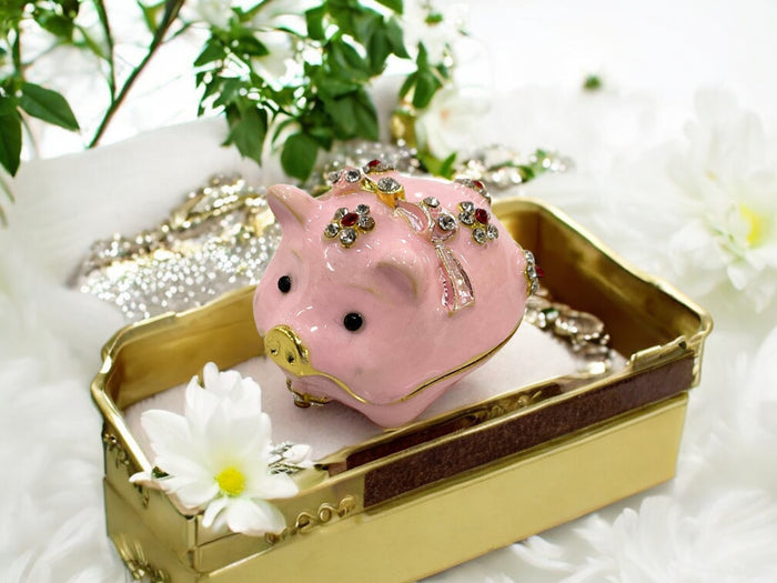 Pink enamel jeweled pig trinket box with rhinestone flower clusters displayed on a white cloth with soft pink floral background