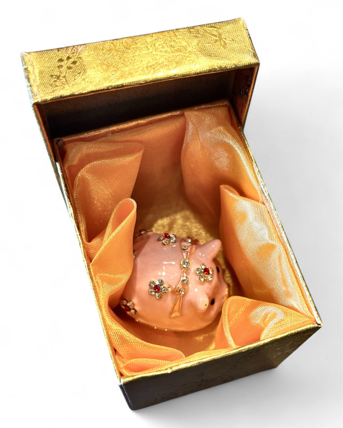 Pink enamel pig trinket box open showing warm amber interior and hinged closure, white background