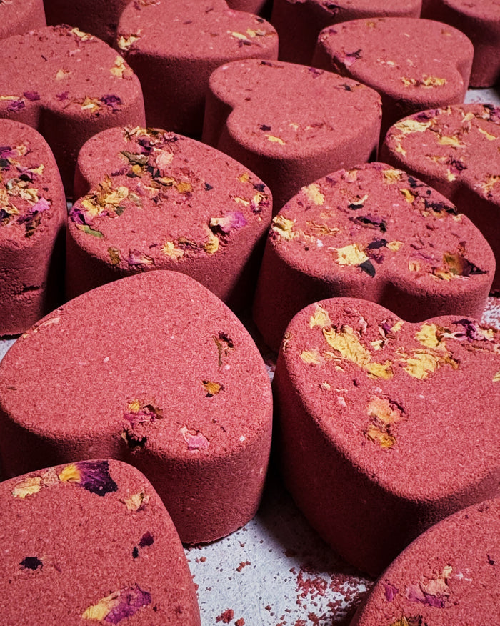 Heart-shaped bath bombs with a textured, dusty rose-pink surface and dried flower petals, arranged closely together.