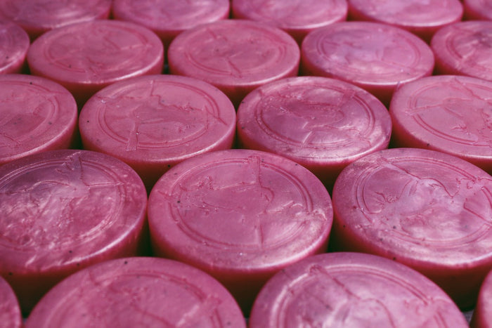 A close-up, top-down view of multiple round pink soap bars arranged in a grid. Each bar has an embossed witch design in the center