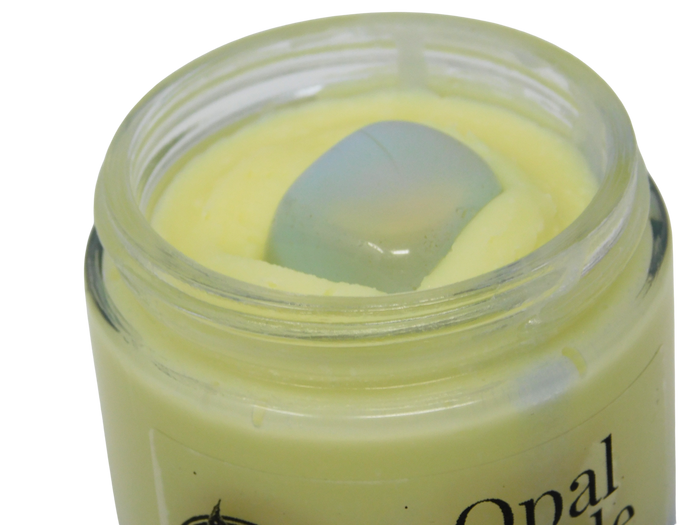 An open clear glass jar containing a pale yellow balm, with a tumbled opal on top. Part of the label reads 'Opal'.