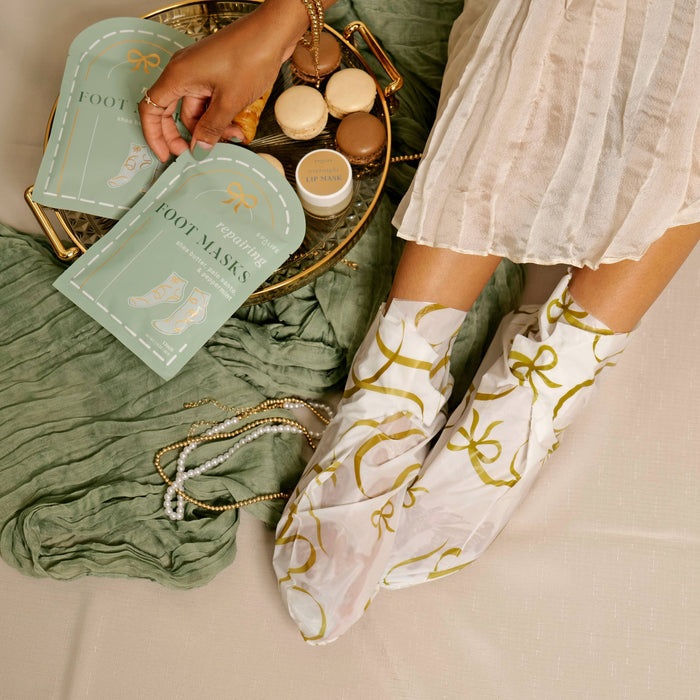 Person wearing white socks with gold bows, surrounded by foot care products on a green towel.