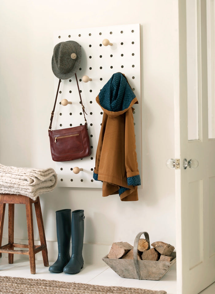 large white pegboard birch plywood in white  by kreisdesign shown in a hallway with hat bag coat hanging on pegboard