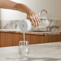Person pouring water from a clear bottle with a white cap into a glass on a marble countertop.