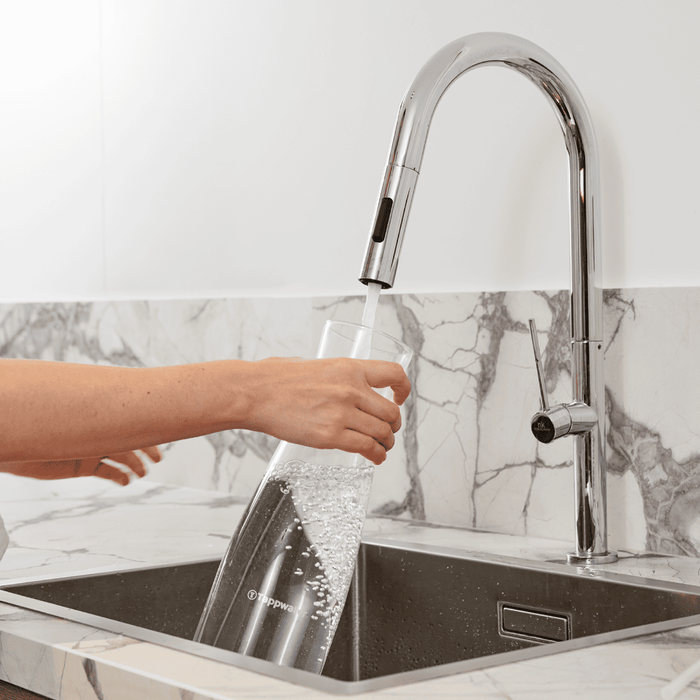 Person washing a glass under a modern kitchen faucet with marble backsplash