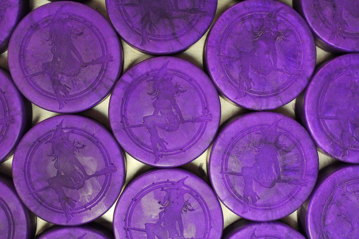 A close-up arrangement of round purple soaps with embossed witches, filling the frame against a light background.
